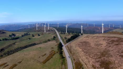 Großer-Windturbinenpark-In-Betrieb-Und-Eine-Zweispurige-Straße,-Die-An-Einem-Sonnigen-Nachmittag-Mit-Blauem-Himmel-Mitten-Durch-Die-Windmühlen-Kreuzt
