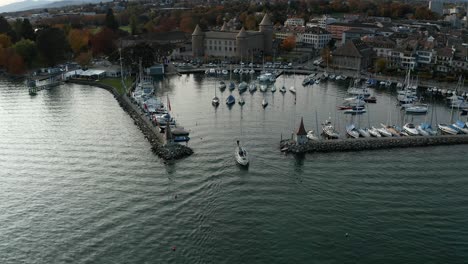 Wide-shot-flyover-drone-shot-of-a-yacht-crossing-the-harbour-entrance-with-a-Swiss-town-in-the-background