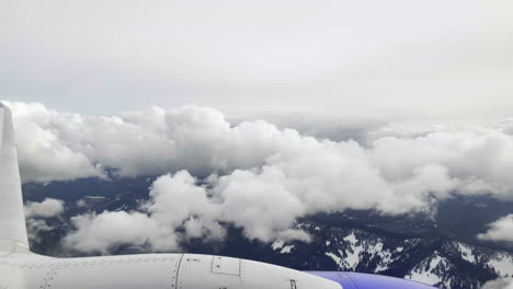 First-person-POV-out-of-an-airplane-window-as-it-flies-over-the-mountains-and-through-white-puffy-clouds
