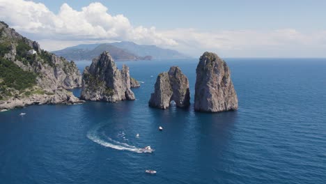 Tourists-Boating-by-the-Epic-Faraglioni-Rocks-off-Capri-Island,-Italy---Aerial