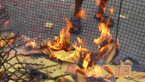 Paper-money-on-fire-inside-caged-fire-pit-with-persons-feet-in-background-during-spiritual-ceremony-to-appease-ancestors-and-ghosts-filmed-in-slow-motion