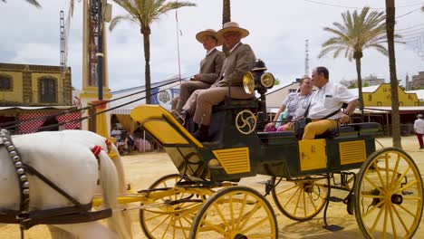 Spanish-couple-rides-in-horse-drawn-cart-with-two-coachmen-at-Jerez-Fair,-SLOWMO