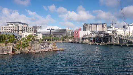 The-beautiful-scenic-Whairepo-Lagoon-and-capital-skyline-of-buildings-and-businesses-on-a-bright-blue-sky-day-in-central-city-Wellington,-New-Zealand-Aotearoa