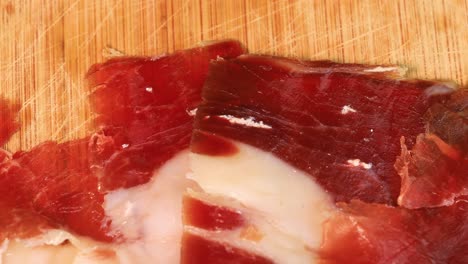 Fatty-prosciutto-slices-rotating-on-a-wooden-board,-macro-shot-in-4k