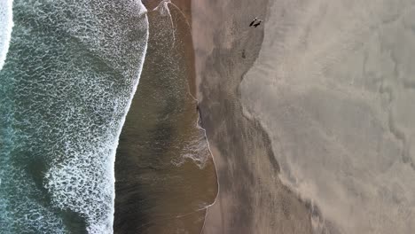 Drone-on-tripod-mode-with-waves-rolling-on-black-sand-beach-below