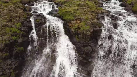 Aerial-close-up-tilting-of-Glymur-waterfalls-streaming-down-steep-rocky-cliff,-in-verdant-highlands-at-daytime,-Iceland