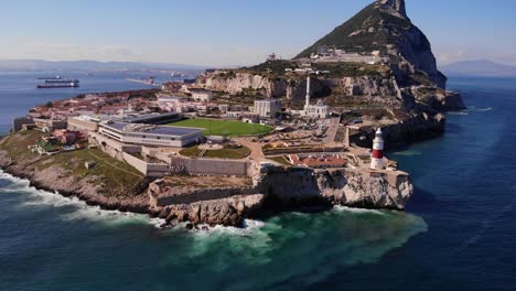 An-Einem-Sonnigen-Tag-Schlagen-Wellen-Gegen-Die-Felsen-Unterhalb-Des-Rot-weißen-Leuchtturms-Am-Europa-Point-In-Gibraltar-Mit-Dem-Oberen-Felsen-Im-Hintergrund-Mit-Toller-Aussicht