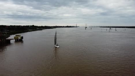 Orbitale-Ansicht-Vom-Dröhnen-Des-Segelboots,-Das-Den-Paraná-Fluss-Mit-Der-Brücke-Im-Hintergrund-Befährt