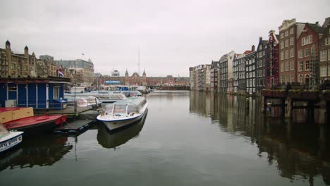 Amsterdam,-Holanda,-Calle-Damrak,-Reflejo-De-Agua-Y-Vuelo-De-Gaviotas,-Tiro-Estático-Ancho-Nublado