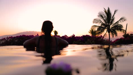 camera-pans-across-infinity-pool-young-tattooed-island-girl-watches-sunset-behind-island