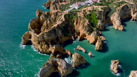 Pan-up-drone-shot-from-the-Algarve-Coast,-revealing-a-lighthouse-on-the-coastline