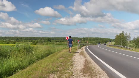 Lonely-Traveler-Walks-Beside-Highway-in-Europe,-Sunny-Summer-Day