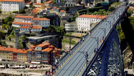 Tourists-crossing-Luís-I-Bridge-with-Crowds-and-Market-Stalls-below,-Porto,-Portugal-4K-SLOWMO-CINEMATIC-AERIAL-SUMMER-MEDITERRANEAN-CITY