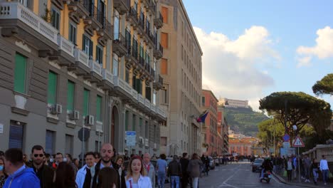 Panning-down-beautiful-street-with-many-people-passing-by-and-stunning-architecture-with-Certosa-e-Museo-di-San-Martino-in-the-background-in-Naples,-Italy