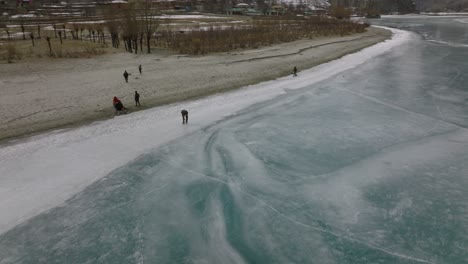 Luftaufnahme-über-Die-Silhouette-Von-Menschen,-Die-Auf-Dem-Zugefrorenen-Khalti-See-Im-Ghizer-Tal-Eislaufen
