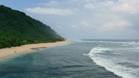 couple-on-empty-white-sand-beach-coastline-in-Uluwatu-Bali-on-sunny-day,-aerial