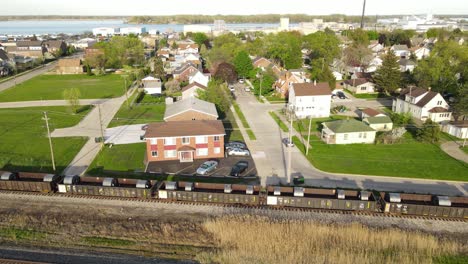Heavy-cargo-train-passing-peaceful-living-district-of-Wyandotte-town-in-Michigan,-aerial-view