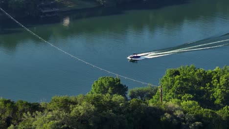 Boat-on-glassy-Lake-Austin-carving-perfect-wake-during-summer-morning-chased-by-aerial-4k-drone