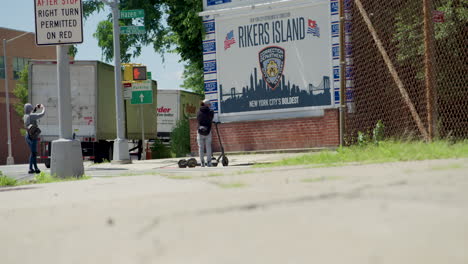 People-On-Electric-Scooters-Take-Picture-In-Front-Of-Rikers-Island-Jail-Sign-In-NYC