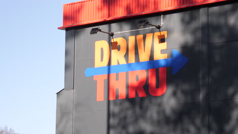 Orange-painted-"DRIVE-THRU"-signage-painted-on-a-building's-wall-in-gray-and-arrow-pointing-towards-the-right-to-the-direction-of-drive-through
