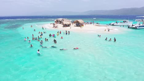 Toma-De-órbita-Aérea-De-Muchos-Turistas-Nadando-Y-Disfrutando-De-Aguas-Cristalinas-Del-Mar-Caribe---Isla-Paraíso,-República-Dominicana