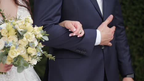 Bride-and-groom-holding-hands-during-outside-garden-wedding-ceremony-close-up-shot,-with-flowers-and-bouquet-in-her-hands