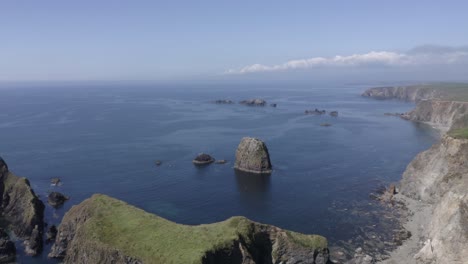 Aerial-flyover-of-sea-stack-rocks-off-rugged-calm-ocean-coastline