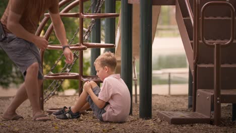 crying-injured-boy-at-park-playgound-braces-knee-injury,-father-comes-to-give-him-a-bandaid-and-help-him-up-on-a-bright-summer-day