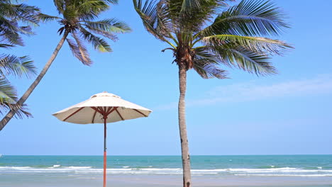 Summer-Breeze-on-Tropical-Destination,-Parasol-Under-Coconut-Trees-and-Sea-Horizon