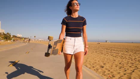 Mädchen-Mit-Sonnenbrille-Mit-Longboard-Beim-Spaziergang-Im-Skatepark-Im-Sommer---Zeitlupe