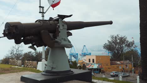 Pan-right-of-an-old-army-machine-gun,-Chilean-flag-waving-in-the-back-in-National-Maritime-Museum,-Valparaiso,-Chile