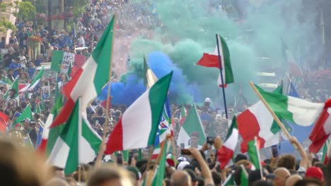 A-huge-crowd-gathers-in-the-street-celebrating-Italy's-win,-EURO-UEFA,-flags-waving,-smoke-bombs