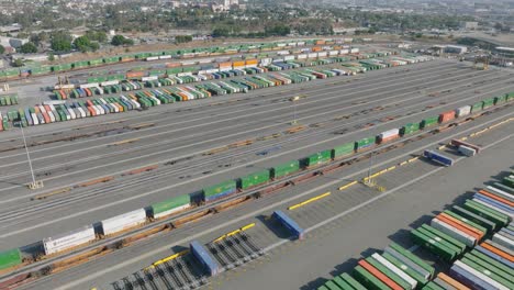 Flying-Above-Train-Yard-in-Los-Angeles,-Lots-of-Colorful-Boxcars-and-Shipping-Containers-Lined-Up