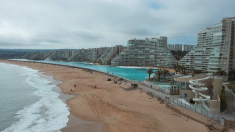 Aerial-pan-right-of-sea-and-sand-shore-near-world-largest-swimming-pool-and-resorts-in-Algarrobo,-Chile