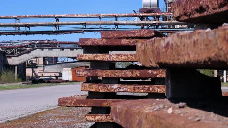 Exterior-view-of-abandoned-Soviet-heavy-metallurgy-melting-factory-Liepajas-Metalurgs-territory,-rust-covered-metal-scrap-piles,-sunny-day,-heat-pipelines-in-background,-medium-shot