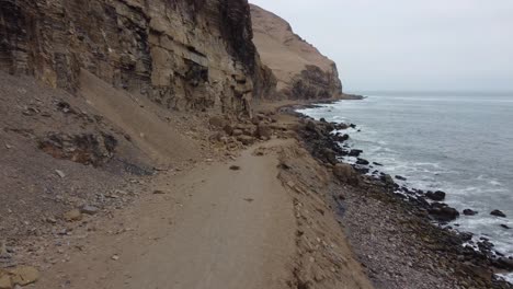 Drone-video-of-person-walking-down-path-next-to-cliff-and-rocky-ocean-shore