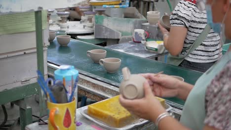 Asiatische-Frau-Verwendet-Pinsel-Mit-Wasser,-Um-Bechergriff-In-Keramikfabrik-Zu-Kleben