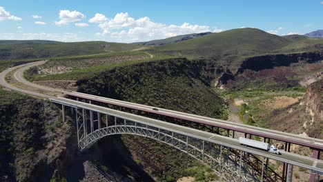4K-drone-pulling-back-over-Burro-Creek-Bridge-in-Wikieup-Arizona-on-a-sunny-day-with-blue-skies-and-patches-of-white-of-white-clouds,-traffic-driving-over-the-bridge