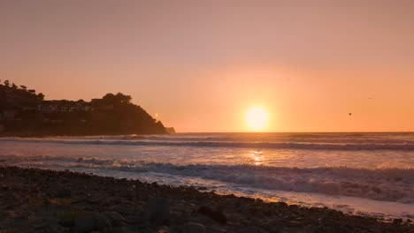Wellen,-Die-Während-Des-Goldenen-Sonnenuntergangs-Mit-Vogelschwärmen-über-Dem-Pazifischen-Ozean-Auf-Die-Felsige-Küste-Treffen