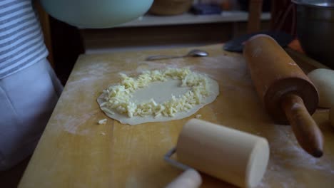 Person-sprinkling-cheese-on-dough-pizza-base-in-home-kitchen