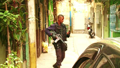 Policeman-in-a-black-uniform-and-armed-with-an-assault-weapon-patrols-an-ally-in-the-favela