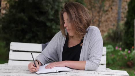 natural-caucasian-women-writes-in-her-journal-sitting-in-the-garden-on-a-white-table
