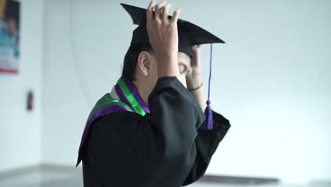 Good-looking-man-in-her-20s-putting-on-a-graduation-cap-and-gown