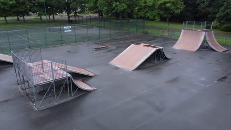 Aerial-view-flying-low-descending-view-across-fenced-skate-park-ramp-in-empty-closed-playground