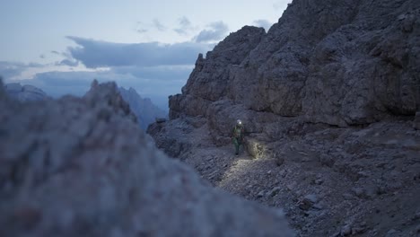 Female-mountaineer-with-headlight-and-climbing-gear-hiking-through-the-Dolomites
