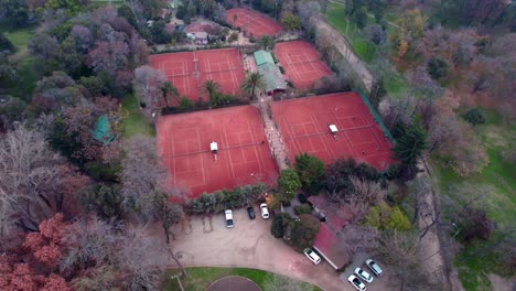 Luftumlauf-Von-Menschen,-Die-Auf-Tennisplätzen-Mit-Rotem-Sand-Spielen,-Umgeben-Von-Bäumen-Und-Vegetation-Im-O&#39;Higgins-Park,-Santiago,-Chile