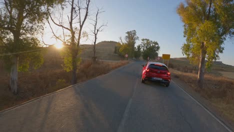 Dynamic-aerial-follows-red-Mazda-car-on-road-through-sun-dappled-trees