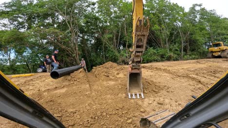 Two-men-maneuvering-a-large-drainage-corrugated-culvert-pipe-into-the-correct-position-in-a-shallow-trench