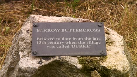Plaque-describing-the-medieval-butter-cross-in-the-middle-of-Barrow-village-in-the-county-of-Rutland-in-England,-UK