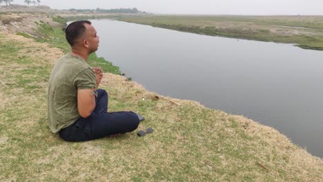 Back-of-a-boy-sitting-in-lotus-pose-in-front-of-the-sea-practicing-yoga-and-praying-in-an-open-field-on-a-summer-morning